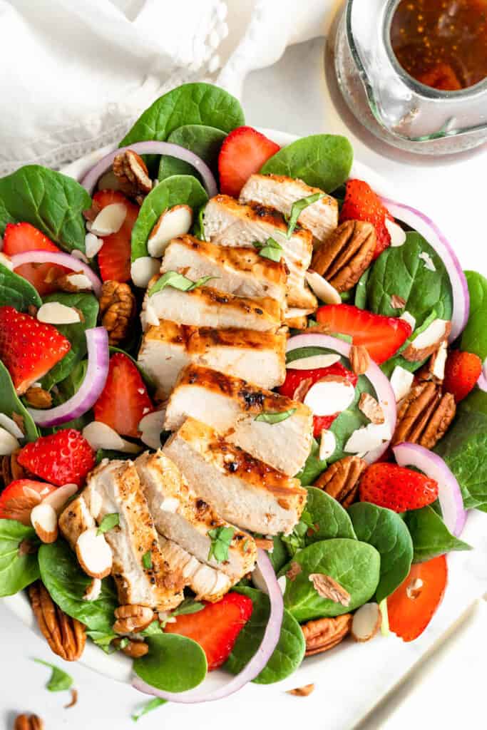 This easy Strawberry Chicken Spinach Salad is a delicious, complete meal! With marinated chicken, strawberries and a homemade vinaigrette! Strawberry Chicken Spinach Salad in bowl topped with pecans.