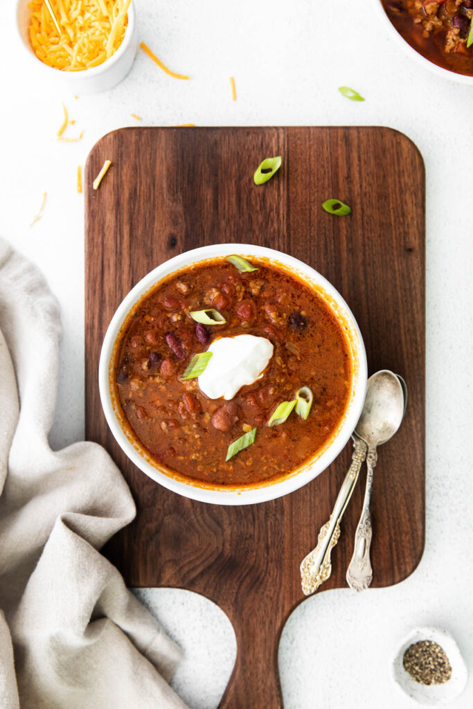 Easy Slow Cooker Chili with homemade seasoning and robust flavor! Packed with protein and perfect for a weeknight dinner! Slow Cooker Chili overhead view with bowl on brown background.