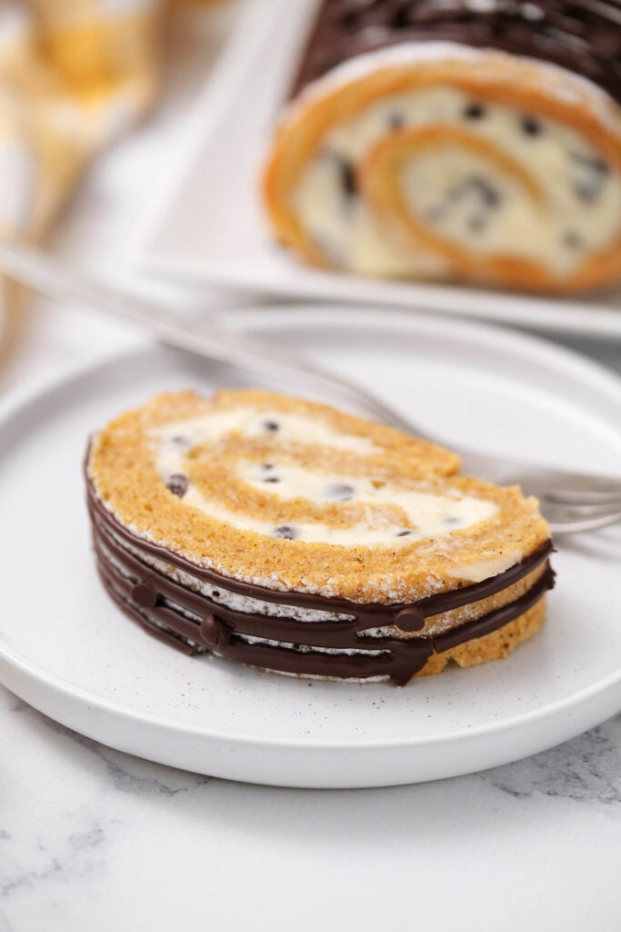 This Chocolate Chip Pumpkin Roll is a fun twist on a classic pumpkin roll! With a fluffy cream cheese filling and mini chocolate chips! slice of Chocolate Chip Pumpkin Roll on white plate.