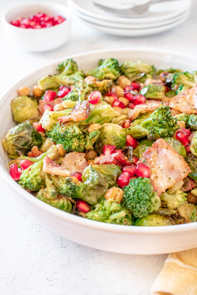This Warm Brussels Sprouts Salad with Bacon, chickpeas and broccoli that is topped with an apple cider dijon dressing! Warm Brussels Sprouts Salad with Bacon in white bowl.