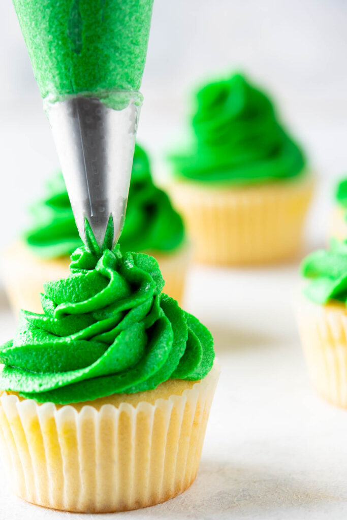 Homemade Christmas Tree Cupcakes that are moist and fluffy! Topped with a festive buttercream frosting! piping green frosting on top of vanilla cupcakes.