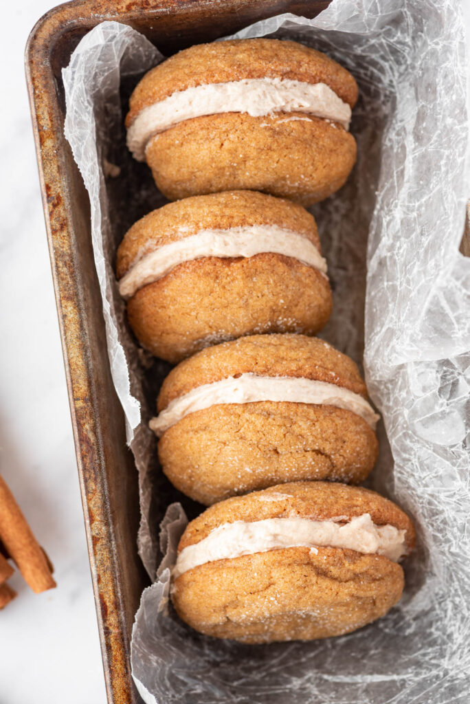 Soft and fluffy Ginger Molasses Cookie Sandwiches! Filled with a cinnamon buttercream frosting! Perfect for any cookie tray! Ginger Molasses Cookie Sandwiches displayed in loaf pan with parchment paper.