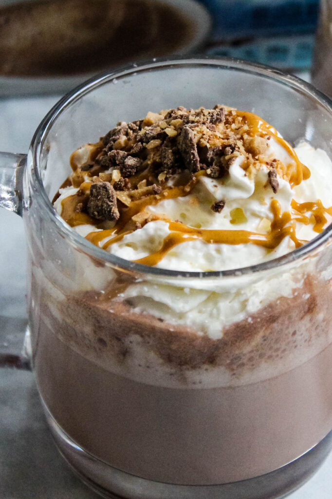 Warm up this season with this easy to make Peanut Butter Hot Chocolate topped with toffee and whipped cream. Perfect for an afternoon treat! Peanut Butter Hot Chocolate in glass mug.