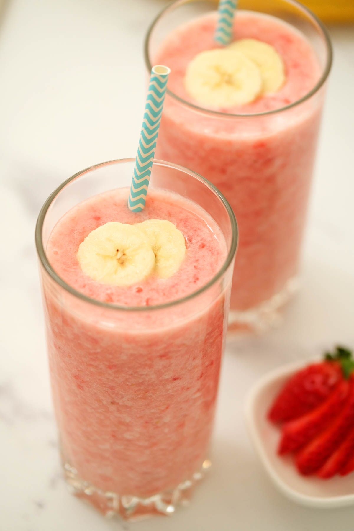 Strawberry Banana Smoothie is so creamy and delicious! Full of strawberry flavor with a touch of banana! Makes for a perfect post workout treat! Strawberry Banana Smoothie in glasses topped with fresh bananas.