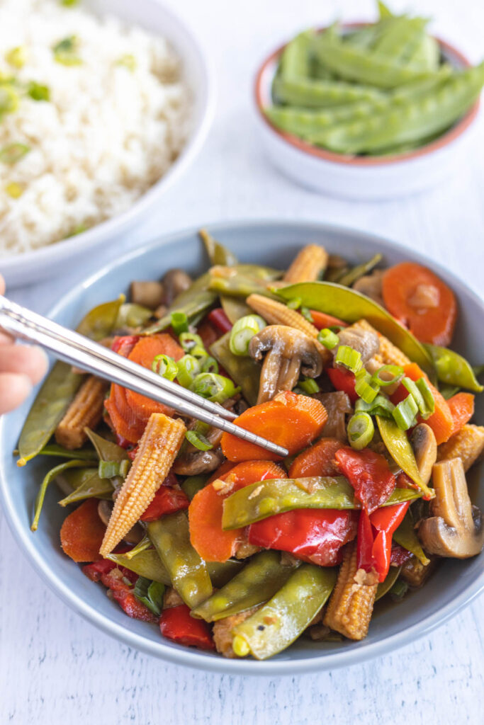 Easy Instant Pot Vegetable Stir Fry filled with hearty vegetables, covered in a sweet and savory sauce. picking up stir fry with chop sticks.