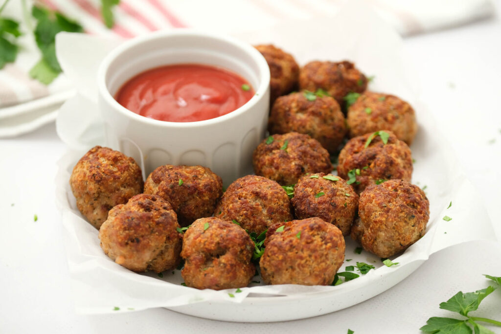 Air Fryer Turkey Meatballs are simple to make and baking up in 20 minutes! Air Fryer Turkey Meatballs on white plate with sauce.
