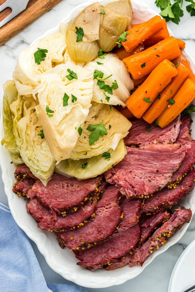 Easy Instant Pot Corned Beef is perfect when you don't want to wait around the oven for hours on end! It's cooked to perfection every time! instant pot corned beef sliced on white plate with veggies.
