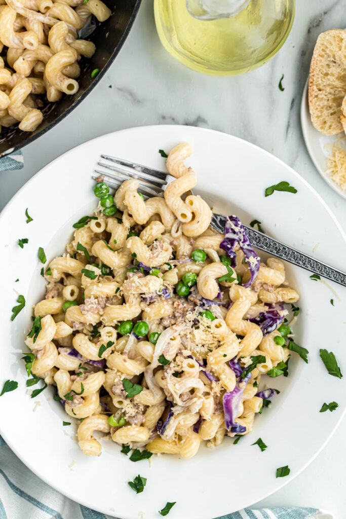 Easy Pasta with Sausage and Radicchio! Made with either penne or cavatappi, filled with vegetables and a cream sauce! pasta with sausage on white plate with fork.