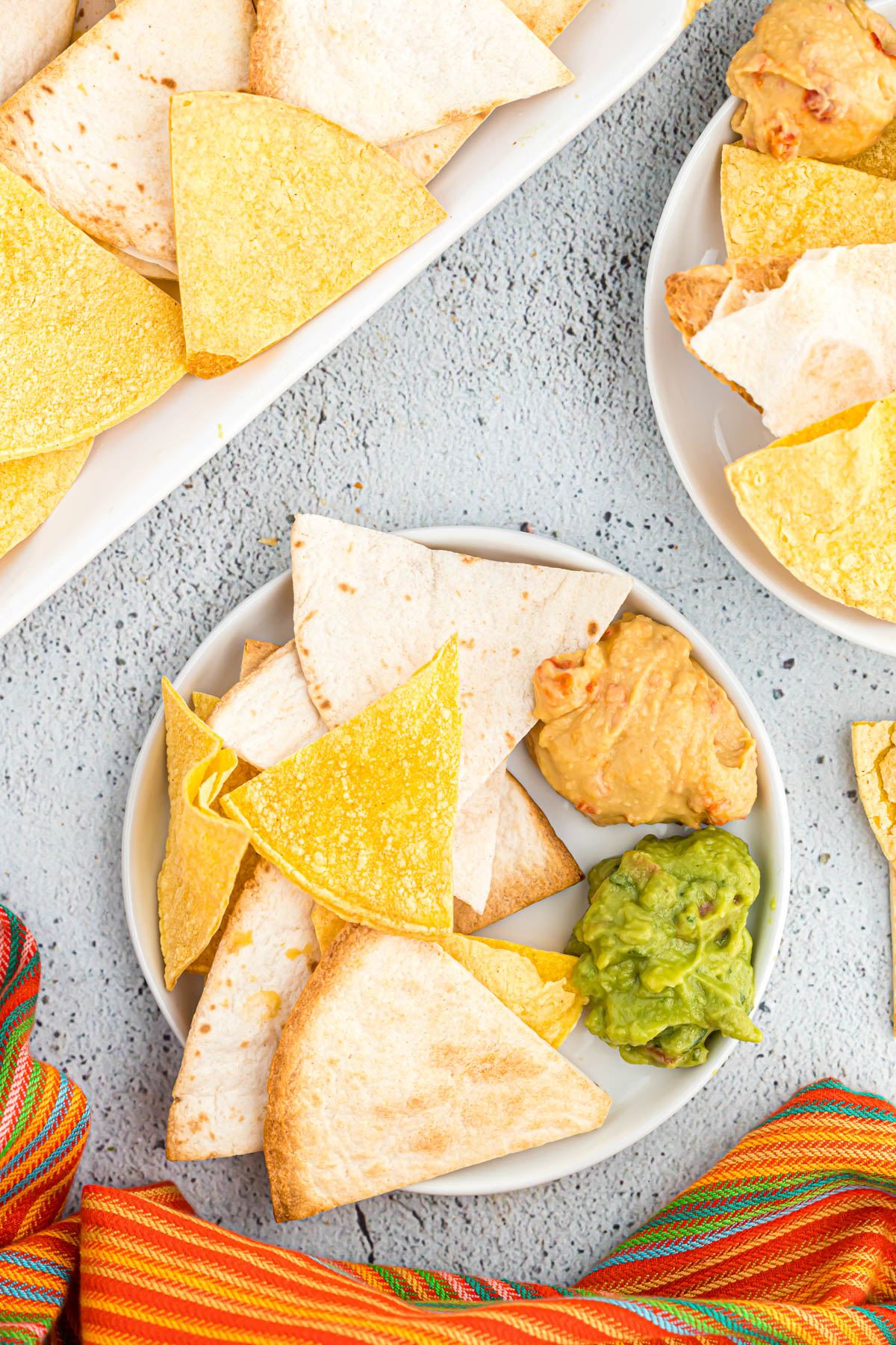 These Air Fryer Tortilla Chips made two ways! Using flour or corn tortilla chips, you can have freshly cooked chips in just minutes! chips on plate with guacamole and hummus.