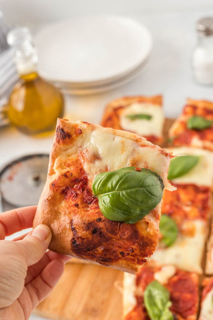 This easy Sheet Pan Margherita Pizza will be your go-to for pizza night! holding a piece of pizza.