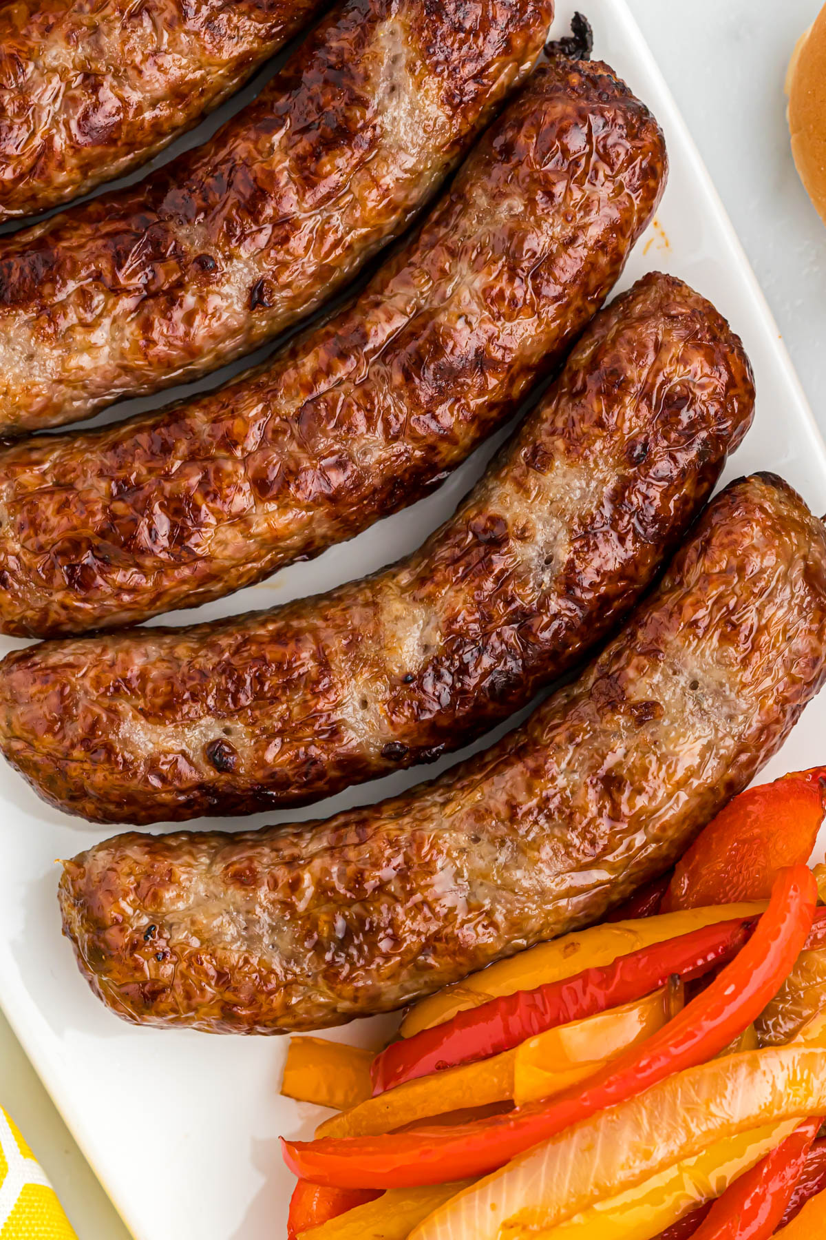 Quick and easy Air Fryer Bratwurst. Loaded with bell peppers and onions in a warm bun, topped with yellow mustard cooked bratwurst on white tray.