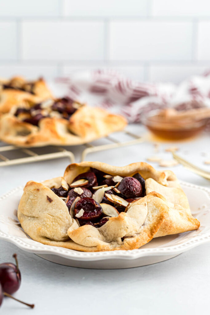 Mini Cherry Almond Galettes are the perfect individual desserts! Filled with fresh cherries, honey and almonds. Baked to perfection! Mini Cherry Almond Galettes on white plate.