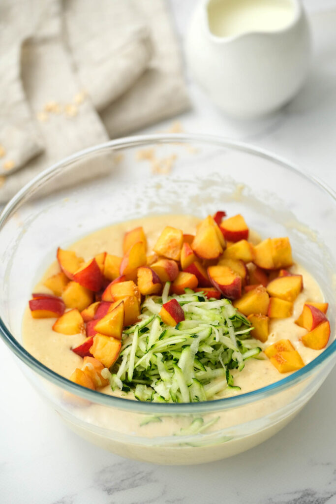 peach and zucchini in glass bowl with muffin mixture.