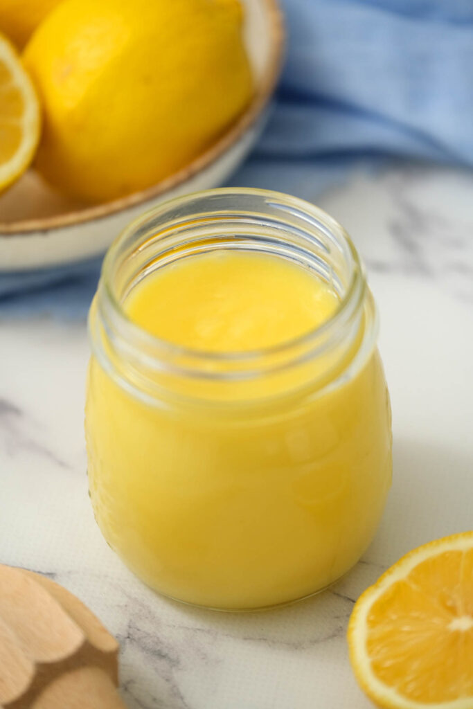 Easy Homemade Lemon Curd! Made with 5 simple ingredients, for a slightly sweet and tart dessert topping or spread! Homemade Lemon Curd in glass jar on white background.