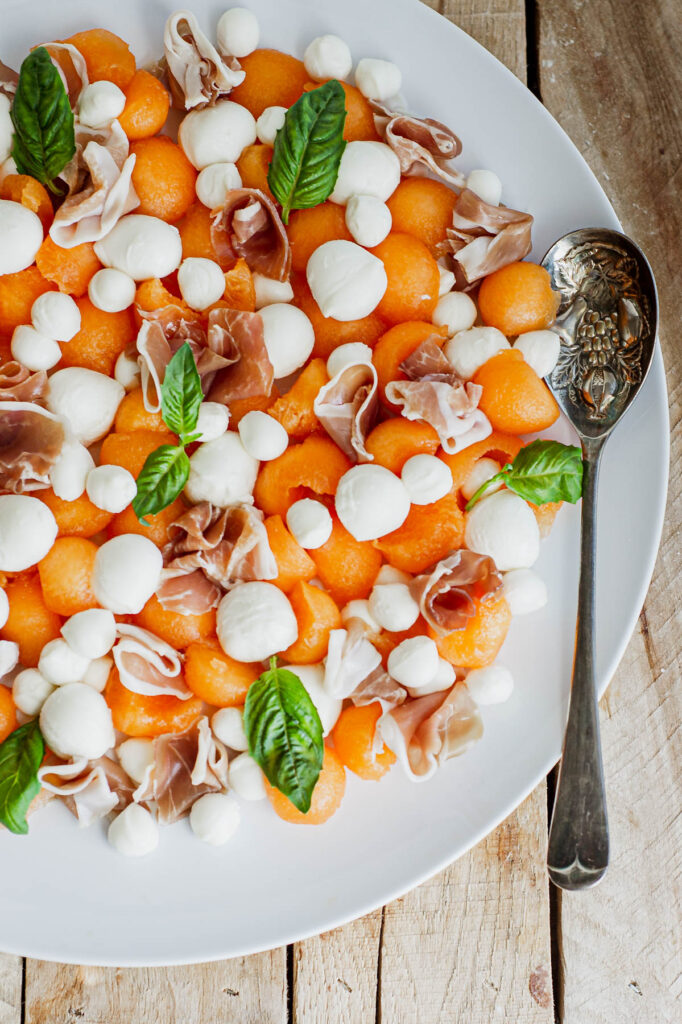 Easy and fresh, Melon Prosciutto Salad! Sweet cantaloupe combined with prosciutto topped with a lemon basil vinaigrette, perfect for summer! overhead view of Melon Prosciutto Salad with spoon.