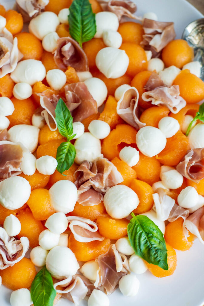 Easy and fresh, Melon Prosciutto Salad! Sweet cantaloupe combined with prosciutto topped with a lemon basil vinaigrette, perfect for summer! Melon Prosciutto Salad on white plate.