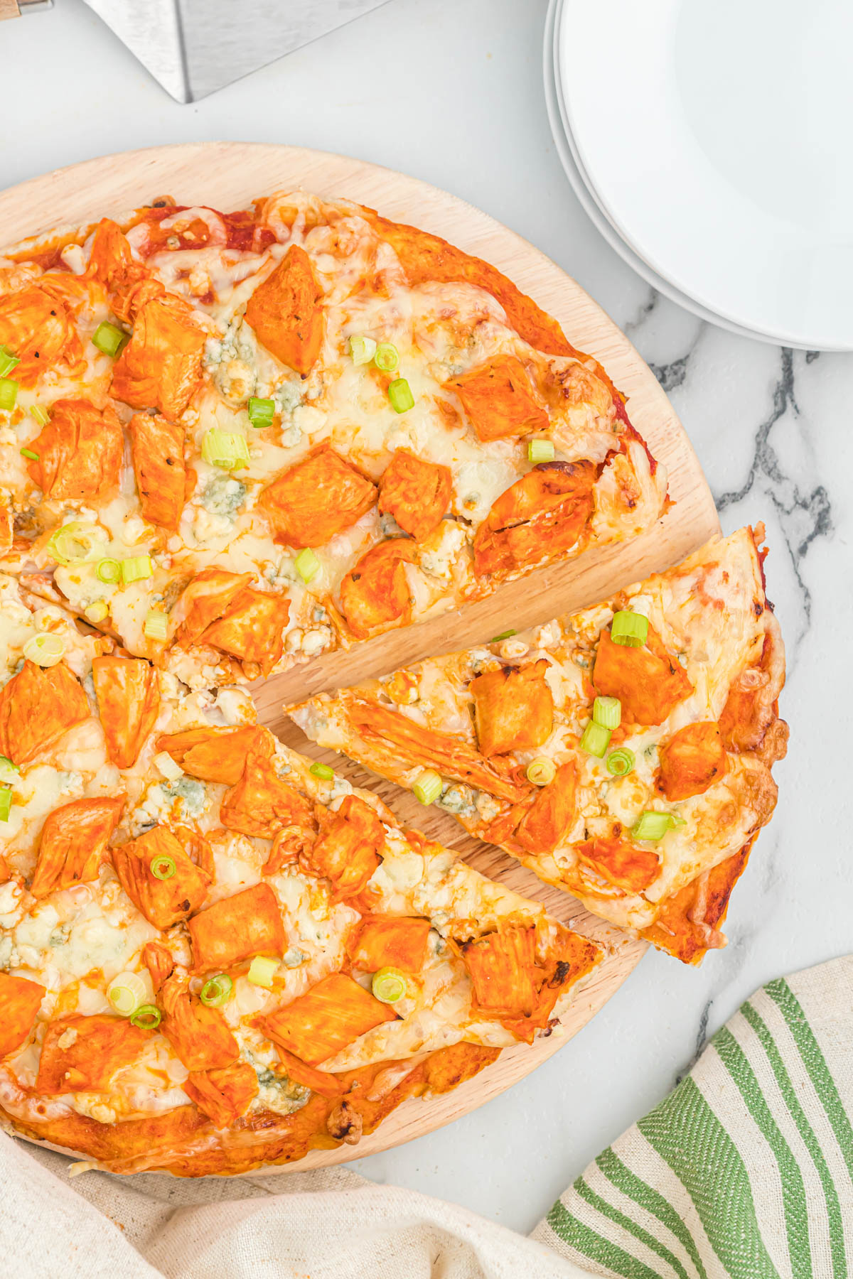 This easy buffalo chicken pizza starts with a homemade pizza dough, topped with chicken, blue cheese, and green onions. slice of pizza cut off the pizza.