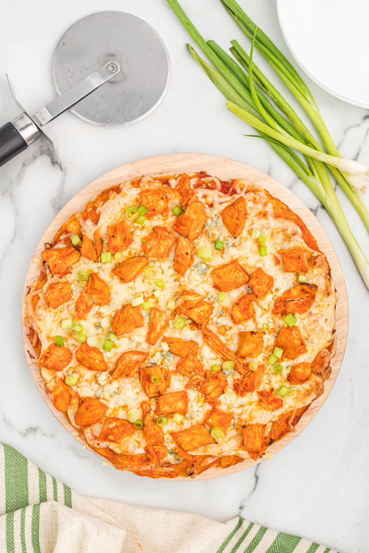 This easy buffalo chicken pizza starts with a homemade pizza dough, topped with chicken, blue cheese, and green onions. pizza with pizza cutter on white back ground.