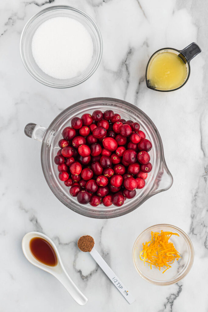 This easy orange cranberry sauce only takes 15 minutes to cook! With a little sweet and tartness this makes for a delicious side dish! ingredients for orange cranberry sauce on white marble background.