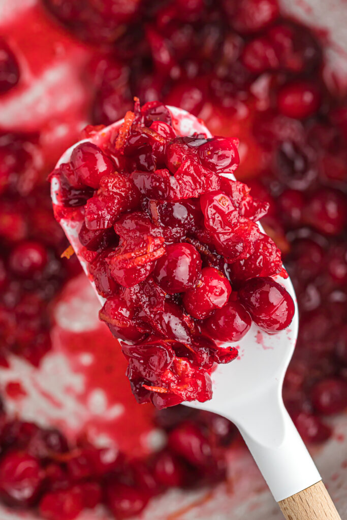 This easy orange cranberry sauce only takes 15 minutes to cook! With a little sweet and tartness this makes for a delicious side dish! cooked sauce on spoon.