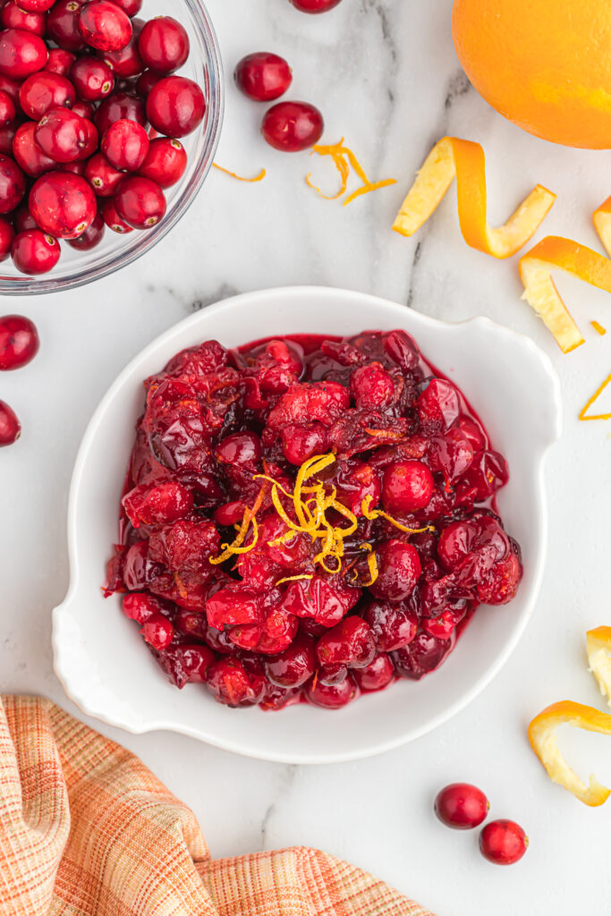 This easy orange cranberry sauce only takes 15 minutes to cook! With a little sweet and tartness this makes for a delicious side dish! cranberry sauce with orange zest on top in white bowl.