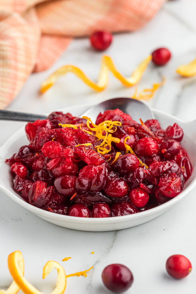 This easy orange cranberry sauce only takes 15 minutes to cook! With a little sweet and tartness this makes for a delicious side dish! orange cranberry sauce in white bowl with spoon.