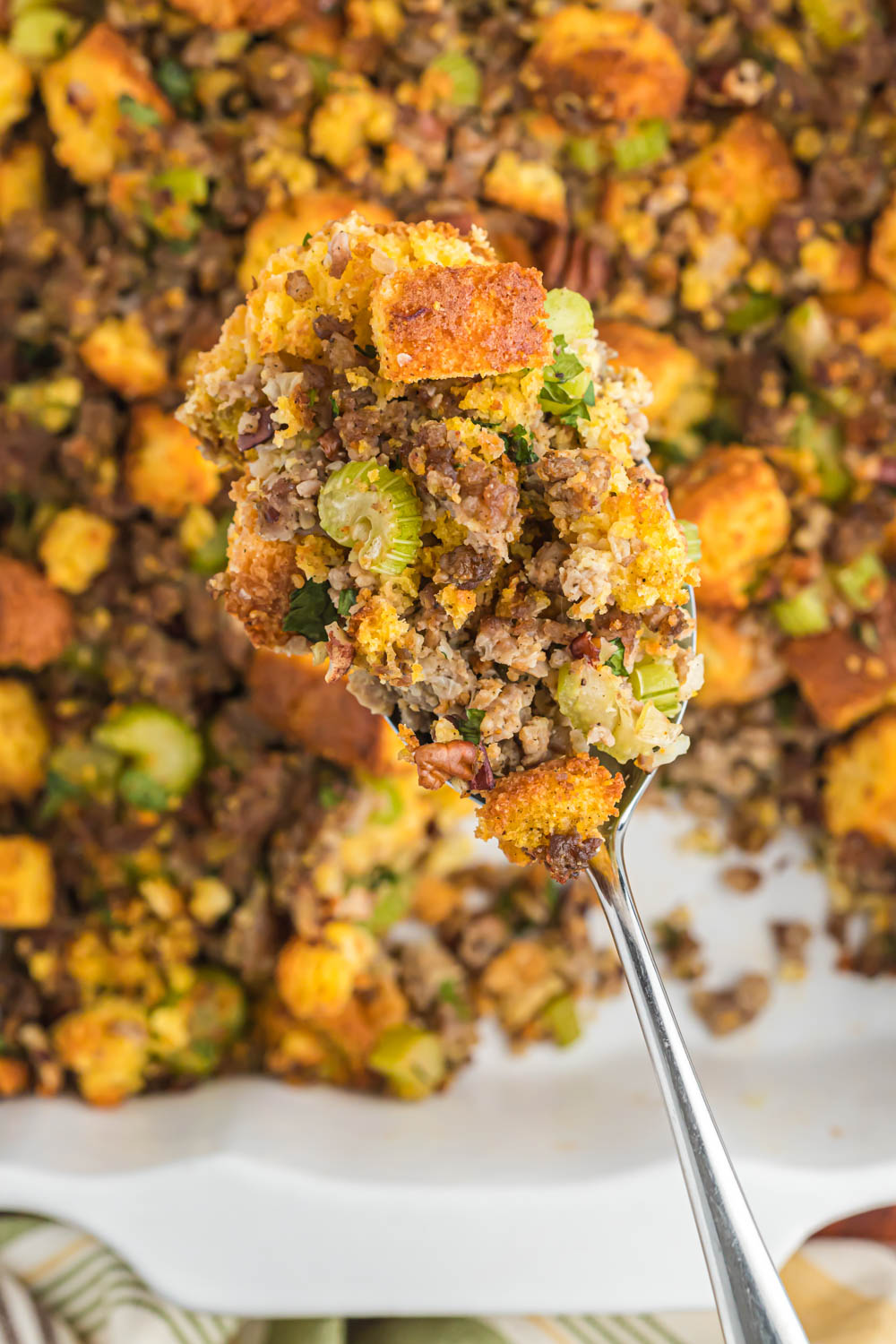 Savory sausage cornbread stuffing, with lots of flavor, seasonings and versatile for any meal with a little added crunch of pecans! stuffing in metal spoon.