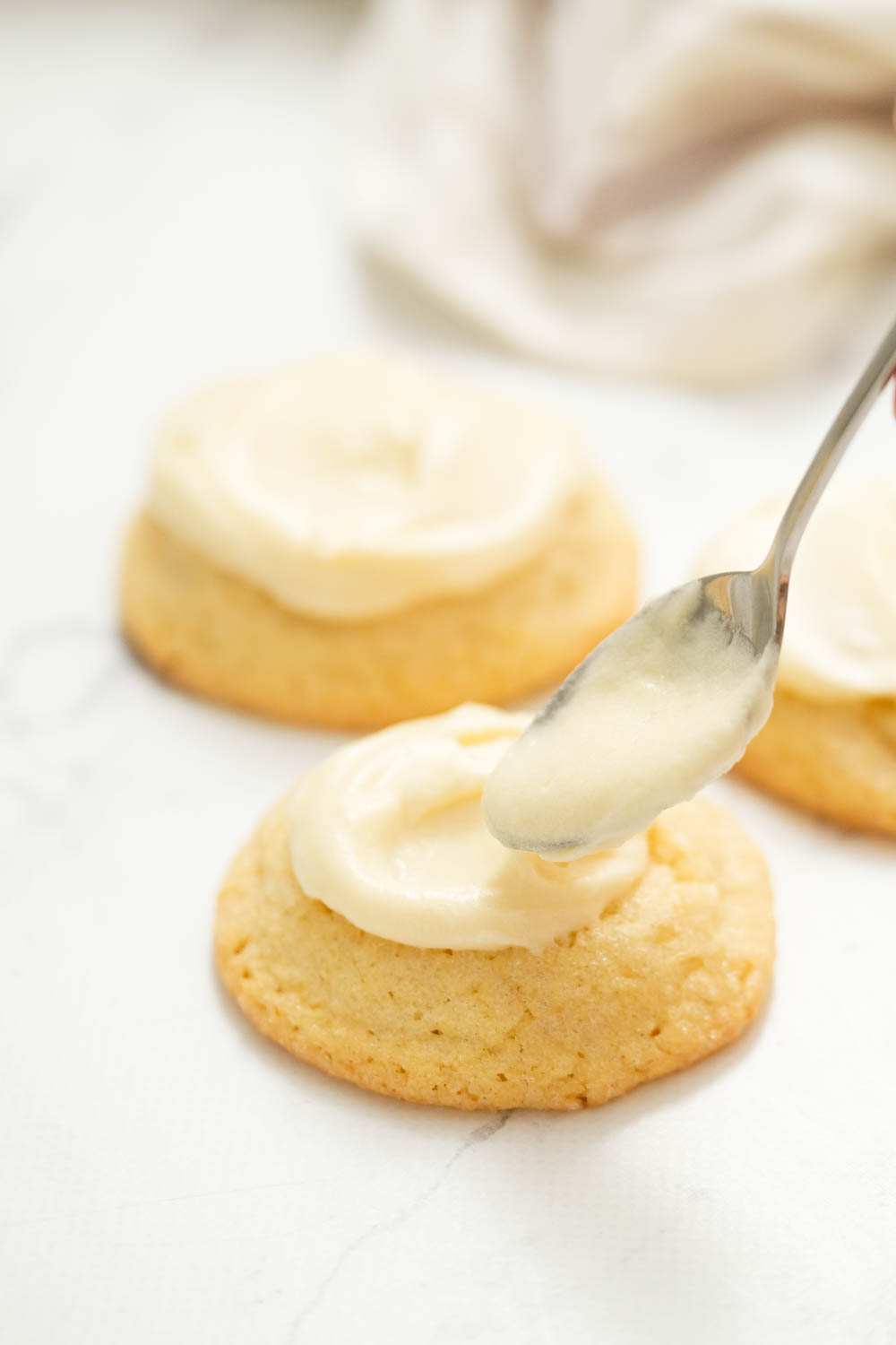 These frosted eggnog cookies are the perfect treat for eggnog lovers! With a touch of nutmeg and topped with eggnog buttercream frosting! adding frosting to cookie with a spoon.