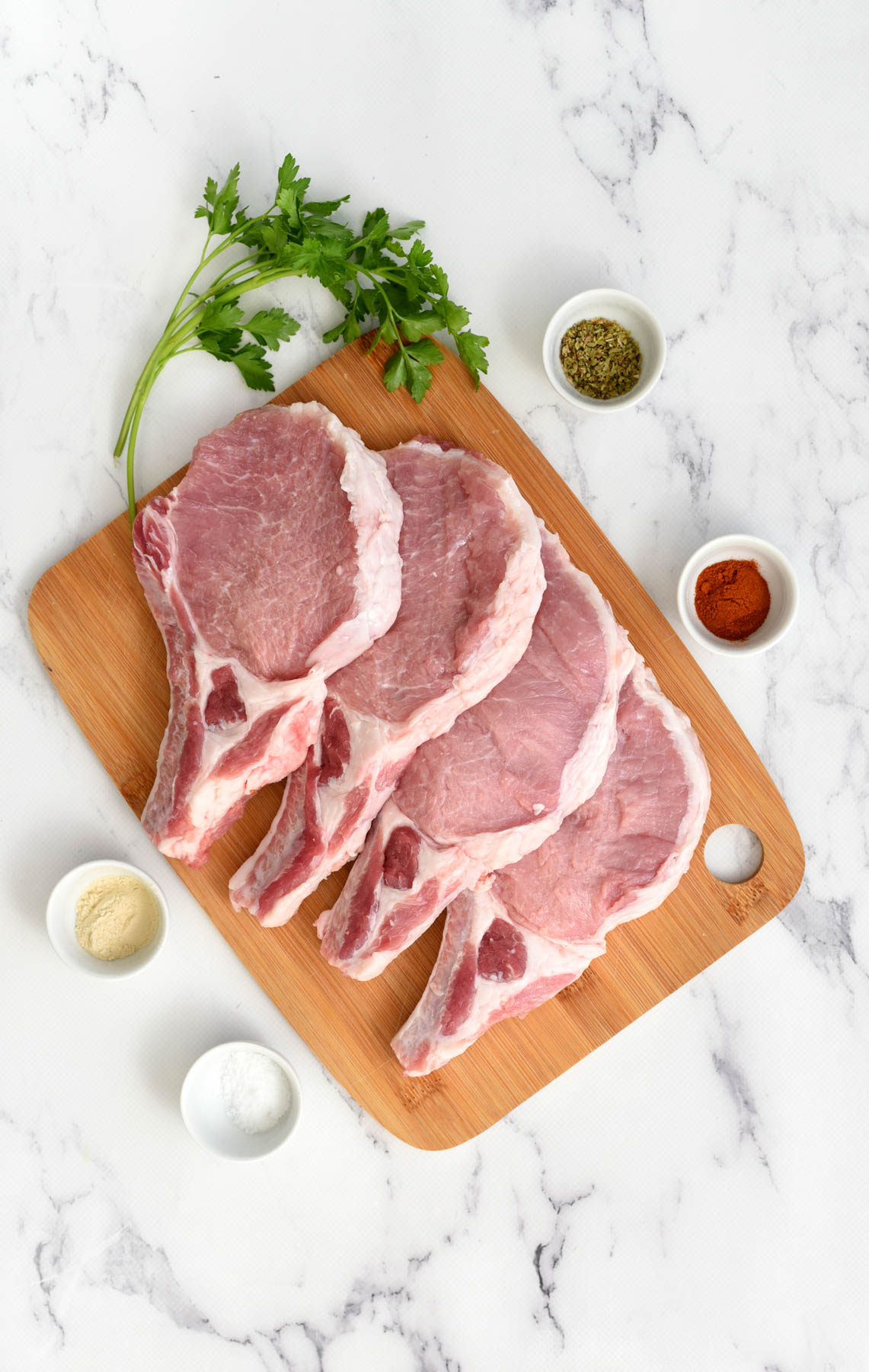 Our recipe for air fryer pork chops is simple and delicious, with crispy golden brown exteriors and tender, flavorful meat inside. ingredients for pork chops on butcher block.