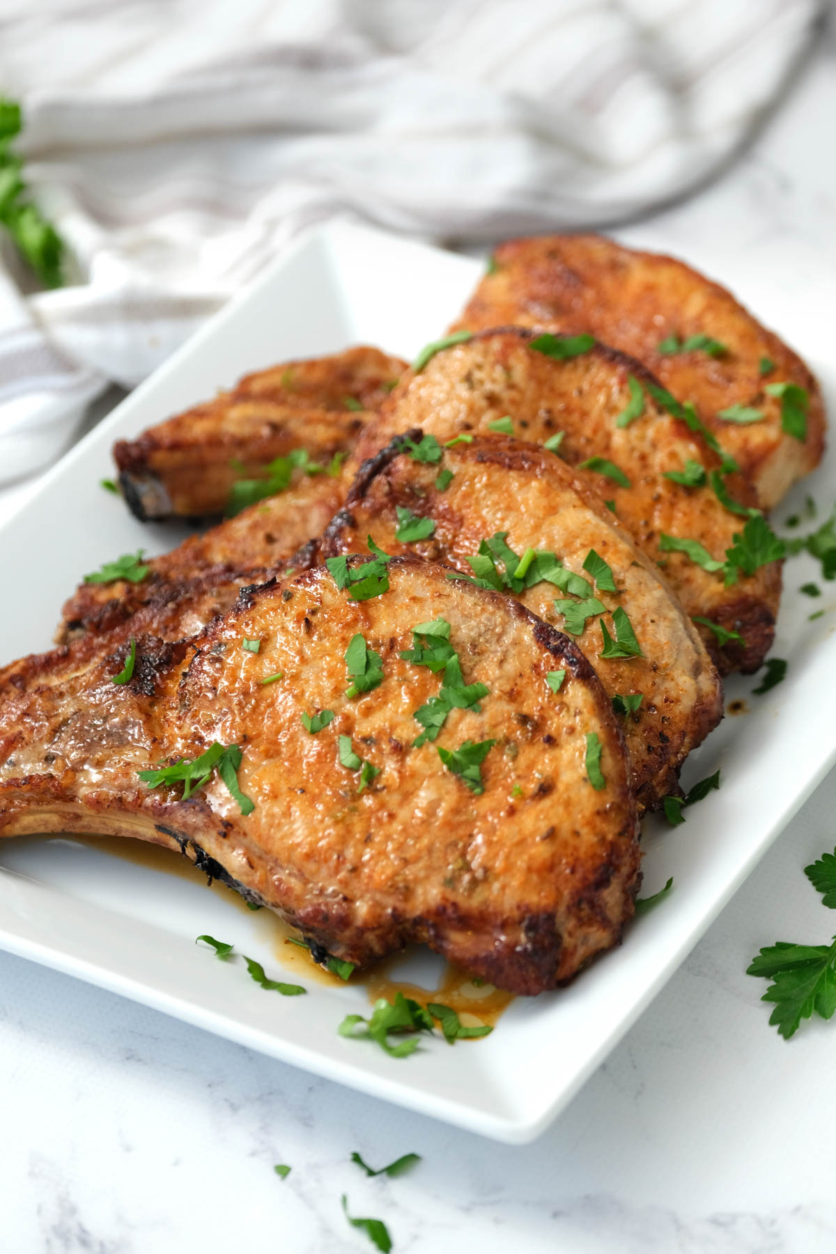 Our recipe for air fryer pork chops is simple and delicious, with crispy golden brown exteriors and tender, flavorful meat inside. cooked pork chops on white plate.
