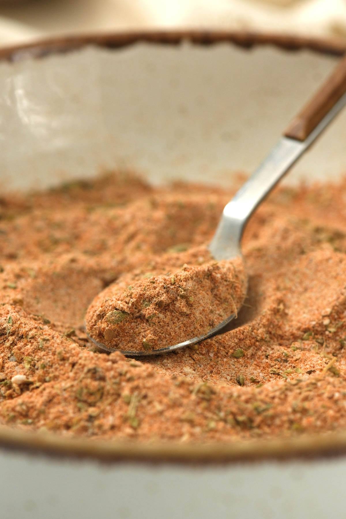 Spice up your meals with our all purpose seasoning blend recipe! Make mealtime more flavorful when cooking up pork, chicken, or veggies! seasoning blend on spoon in white bowl.
