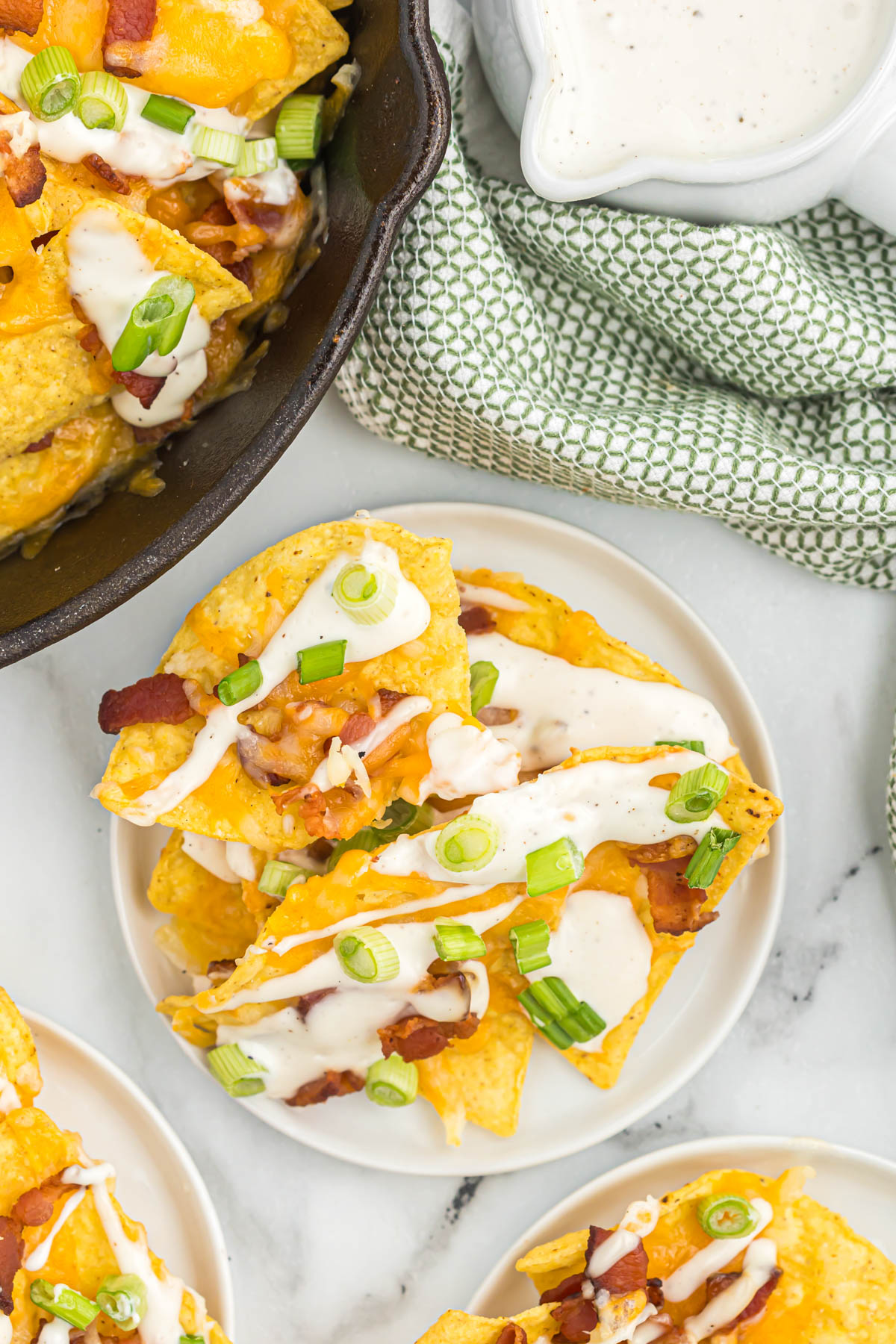 Whip up this quick and easy Bacon Ranch Skillet Nachos recipe in minutes. Crispy tortilla chips smothered in melty cheese, savory bacon, and creamy ranch dressing. bacon nachos on white plate