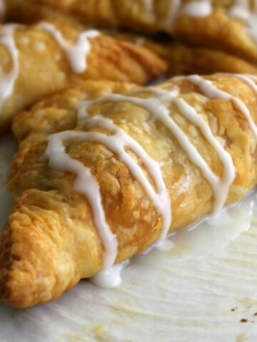 Pumpkin Pie Turnovers on parchment paper with icing drizzled over the top