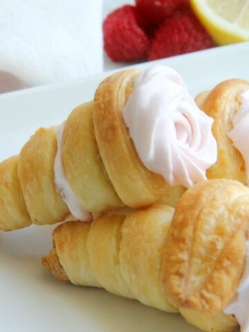 Lemon Raspberry Cream Horns stacked on white plate with raspberries and lemon
