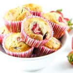 Strawberry Oatmeal Muffins in pink liners stacked in white bowl with fresh strawberries