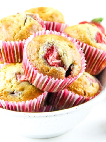 Strawberry Oatmeal Muffins in pink liners stacked in white bowl with fresh strawberries