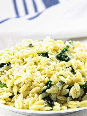 Cheesy Spinach Orzo on white plate with blue and white napkin in the background