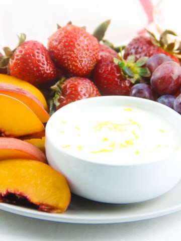 Honey Yogurt Dip in white bowl on grey plate with fresh fruit.