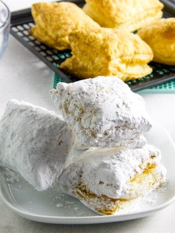 Air Fryer Beignets with tongs and bowl of powdered sugar.