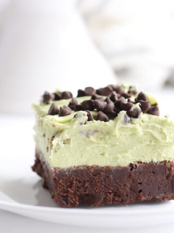 Mint Chocolate Chip Brownies slice on white plate with frosting on top.