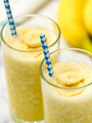 Mango Banana Smoothie in glasses with bananas in background.