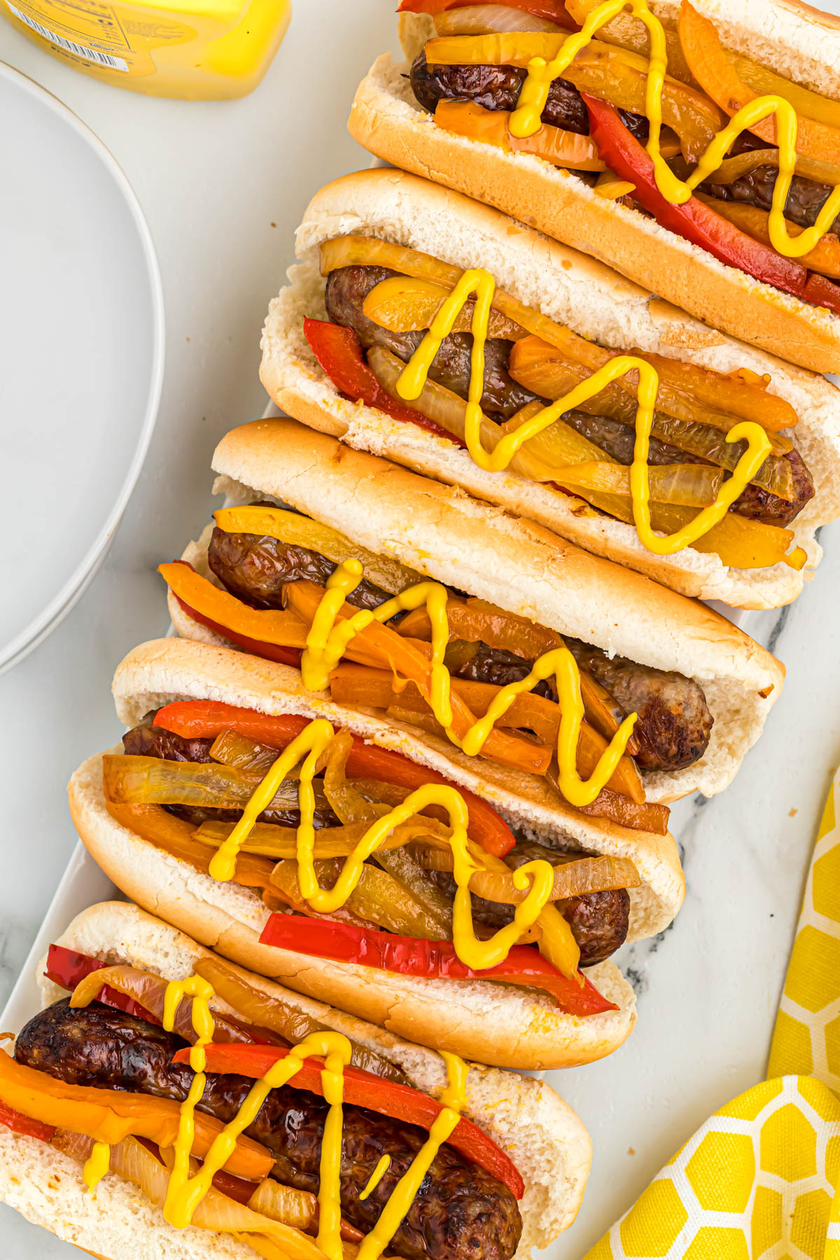 bratwurst in buns topped with peppers, onions, and mustard.